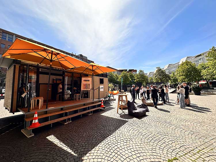 Das Bild zeigt das MobiLab, ein mobiles Mitmachlabor des KIT, auf einem öffentlichen Platz mit einer Gruppe Menschen. 